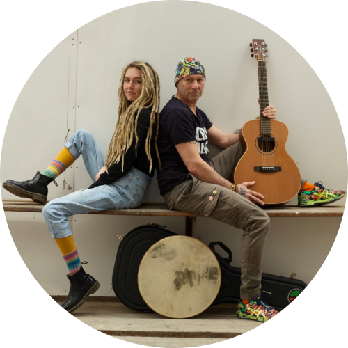 Klaus Zeh und Adeline sitzen auf einer Bank. Klaus Zeh hält eine Gitarre in der Hand.