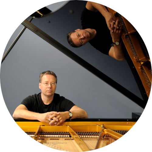 Öffnet die Seite 'Jazz in der vhs' Christ Geisler sitzt am geöffneten Flügel. Sein Bild wird an der Oberfläche des Flügels gespiegelt.