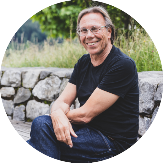 Harald Welzer©Magdalena Türtscher Magma Harald Welzer sitzt mit verschränkten Armen und Beinen lächelnd vor einer Natursteinmauer. Im Hintergrund ist eine Wiese und ein Baum.